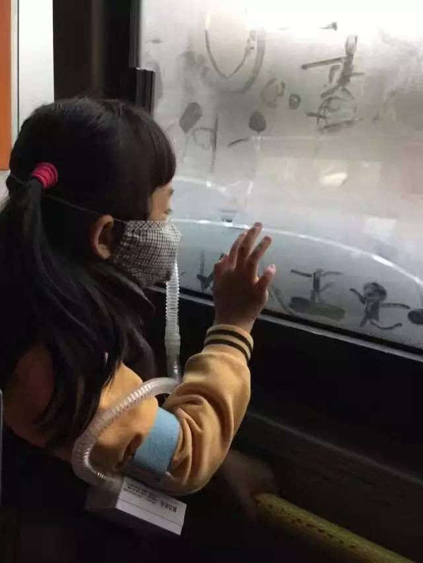 一个戴着便携空气净化装置小学生正在车窗的哈气上画画,画的是正在