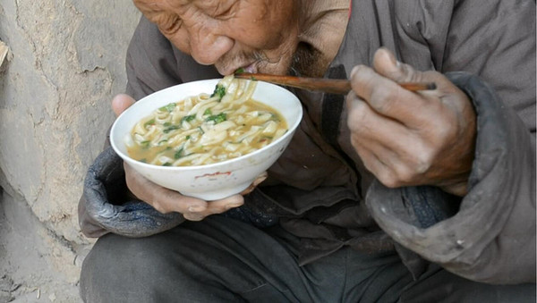 一名刚从地里回来的农村老大爷,蹲在门口吃面.