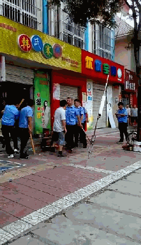 视频中,6名身穿城管制服的男子围在一家店面之前,其中5人手持一根1米